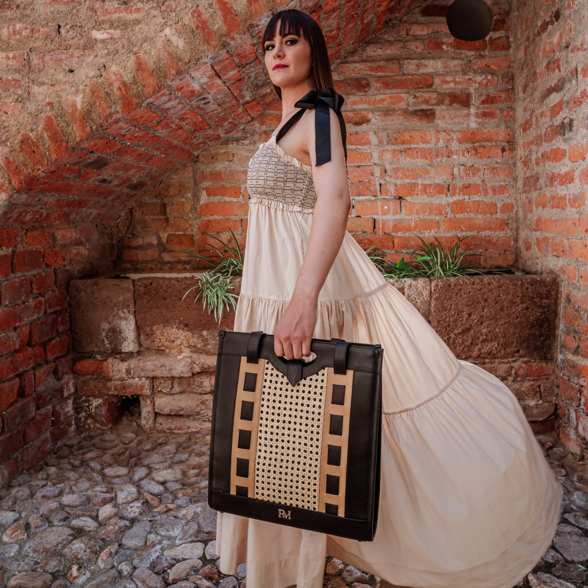 Tote bag with handwoven cane body and black leather trim, open top, structured shape, and dual handles — artisan and elegant.