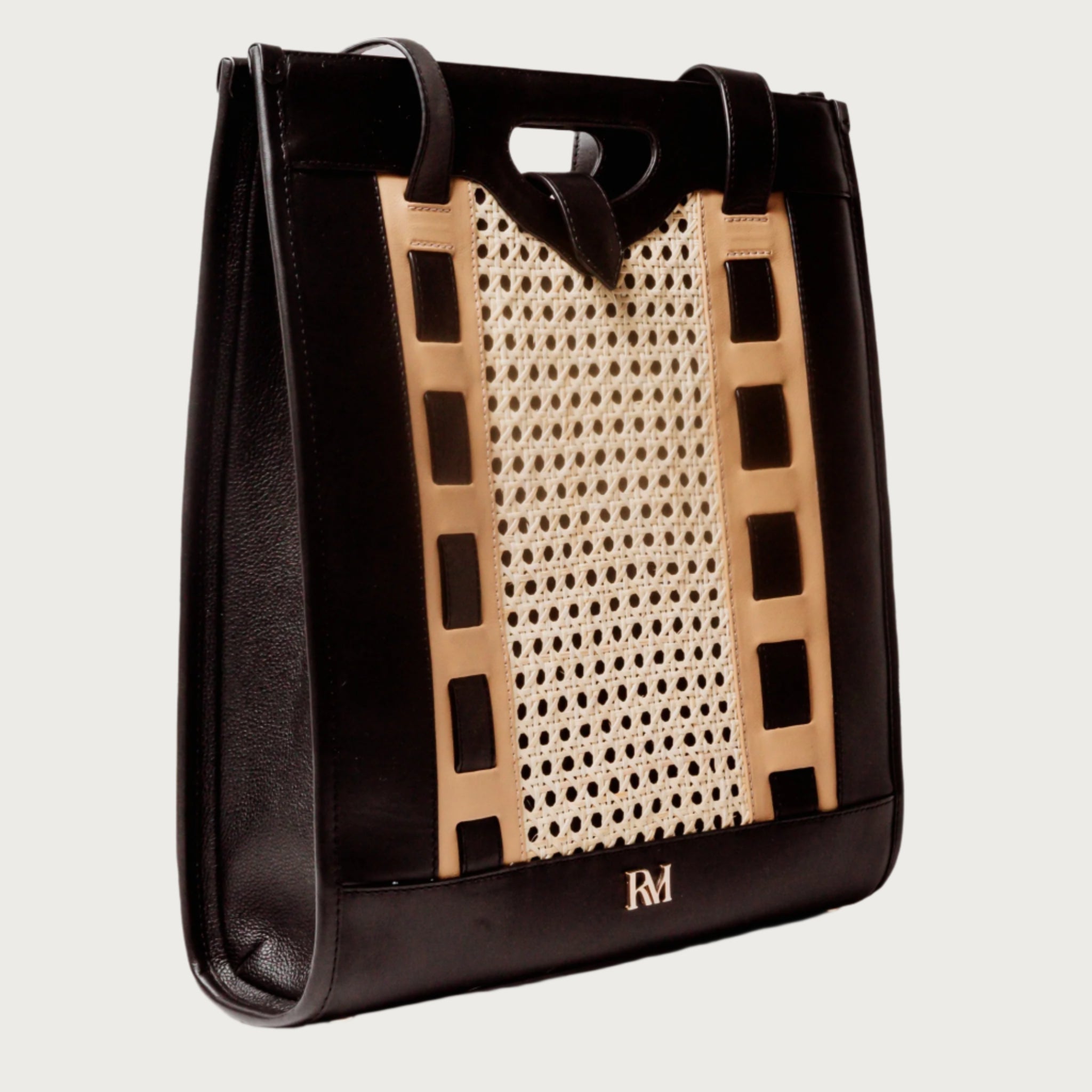 Tote bag with handwoven cane body and black leather trim, open top, structured shape, and dual handles — artisan and elegant.