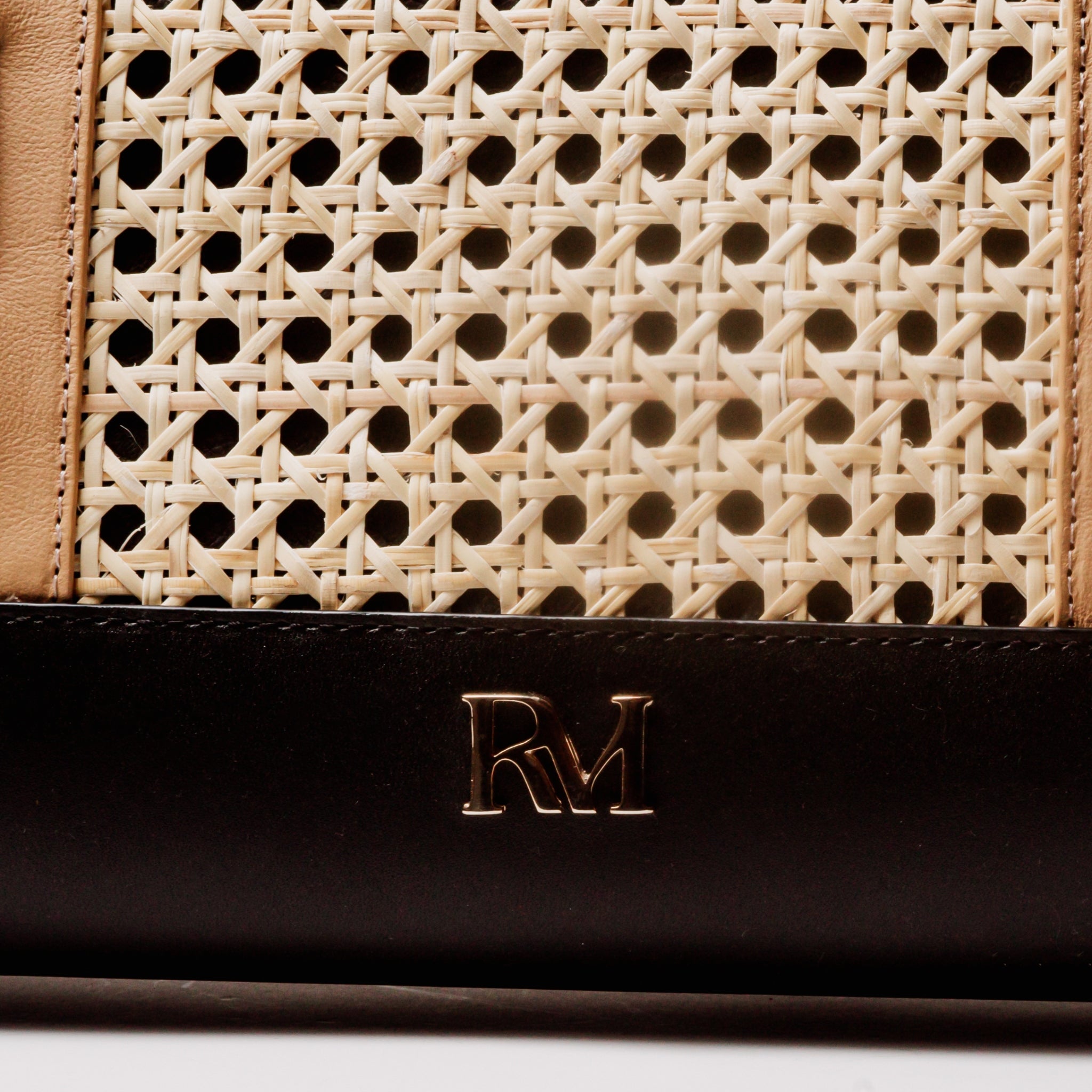 Tote bag with handwoven cane body and black leather trim, open top, structured shape, and dual handles — artisan and elegant.