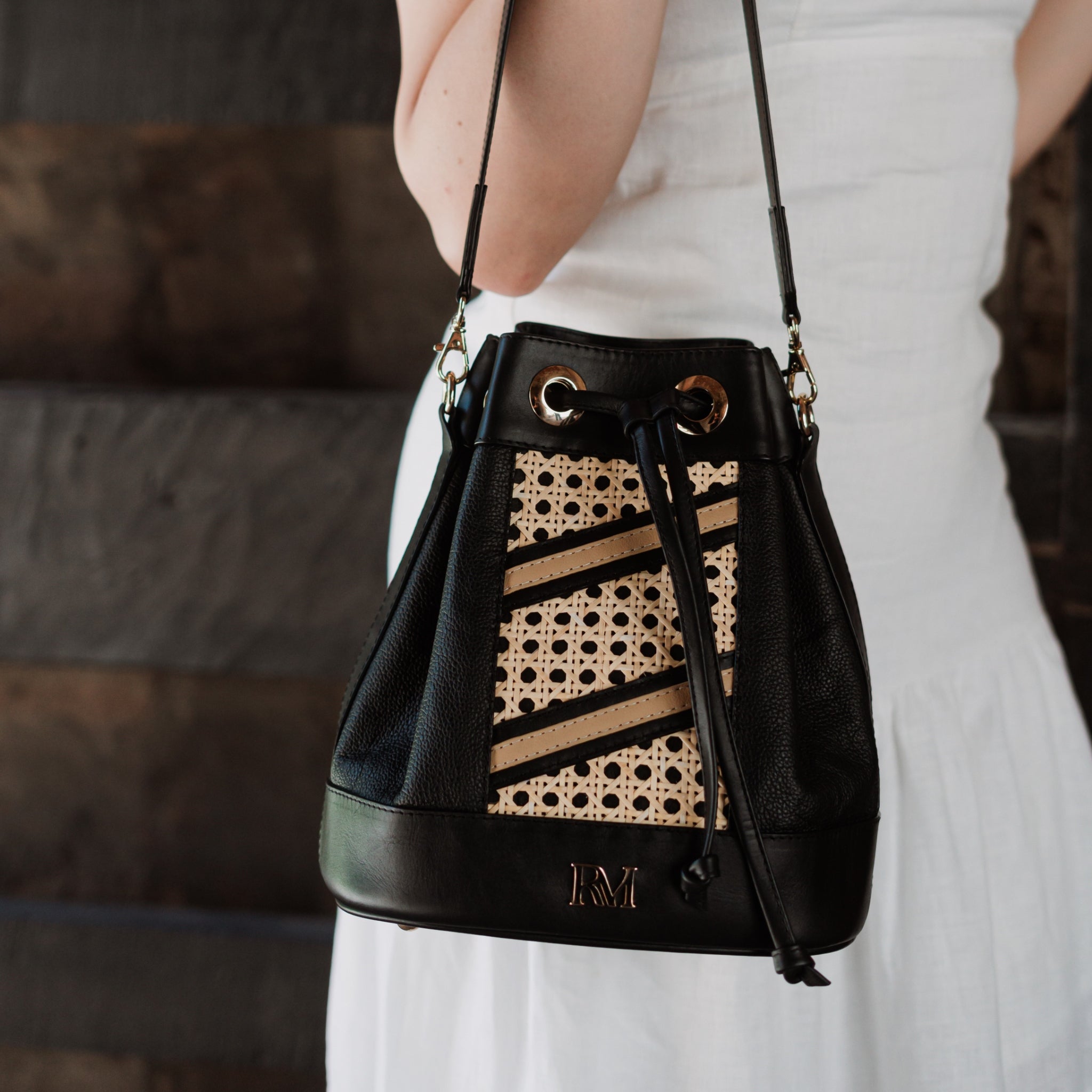 Wicker and black leather bucket bag with drawstring closure, gold hardware, inner lining, and artisan-made woven structure.