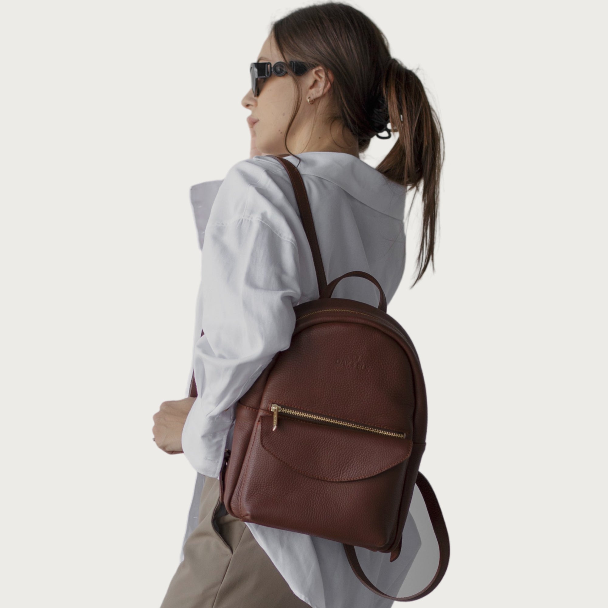 Leather backpack with smooth finish, adjustable straps, front zipper pocket, and gold hardware – Emma by OAK & ELK.