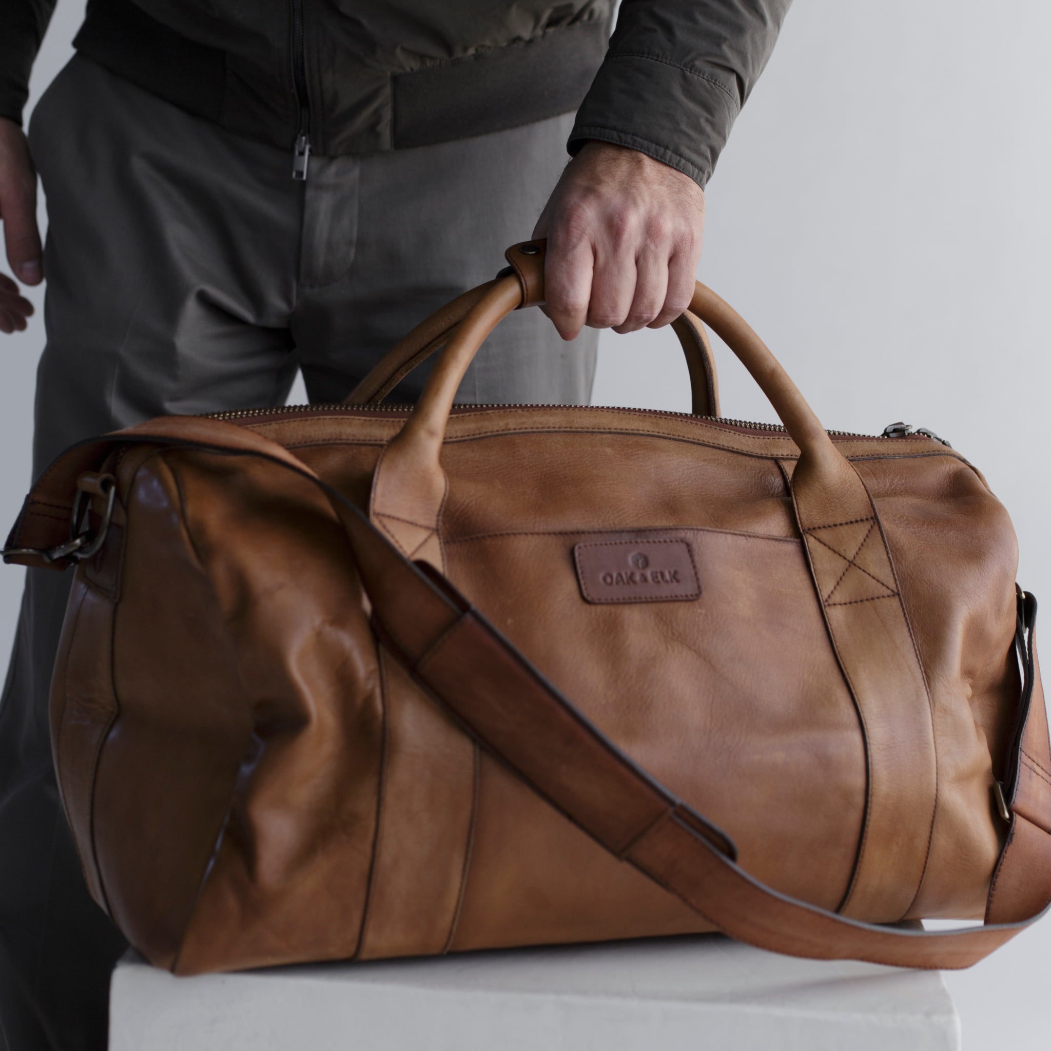 Leather duffel bag made of top-grain leather with smooth zipper, structured body, interior pockets, and adjustable strap
