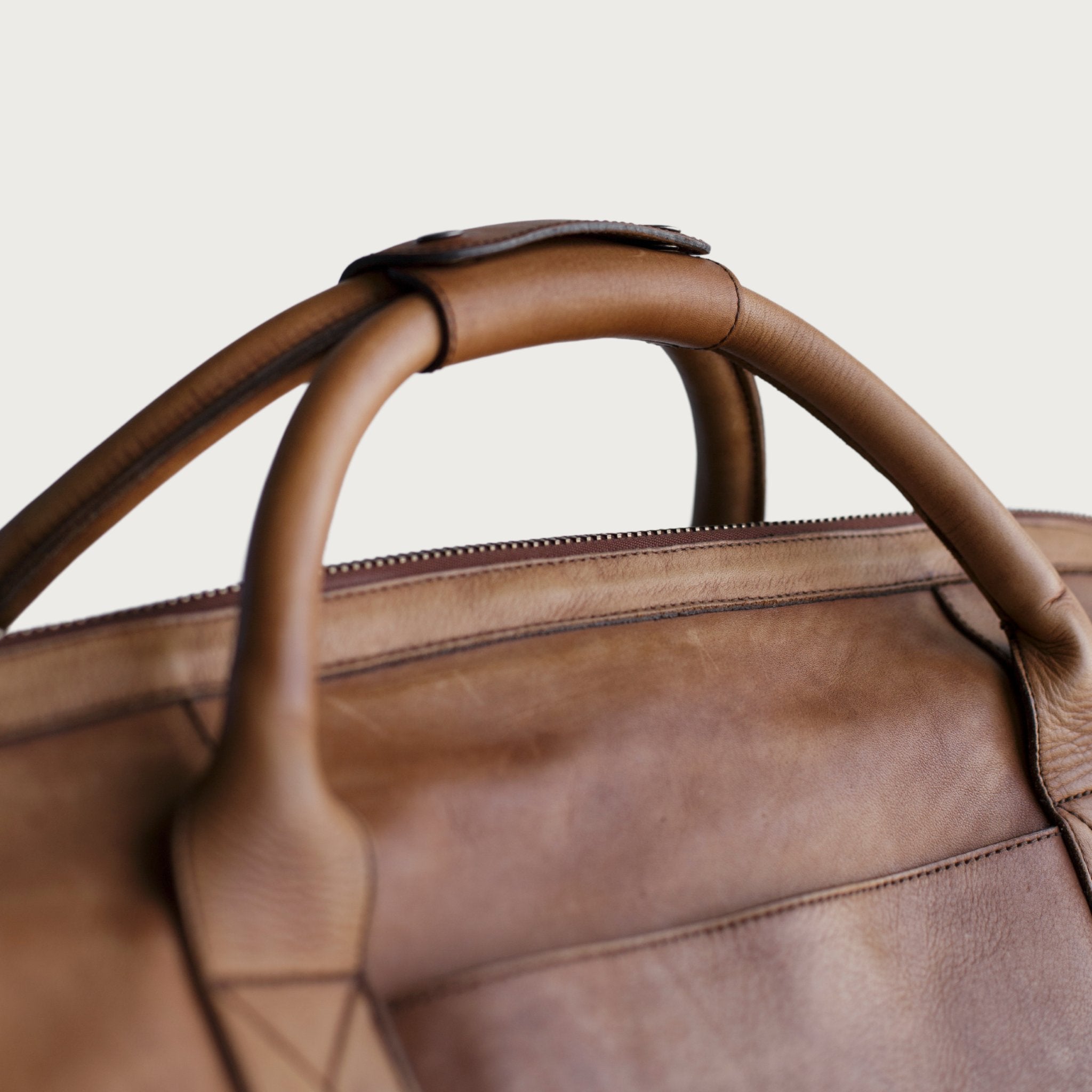 Leather duffel bag made of top-grain leather with smooth zipper, structured body, interior pockets, and adjustable strap