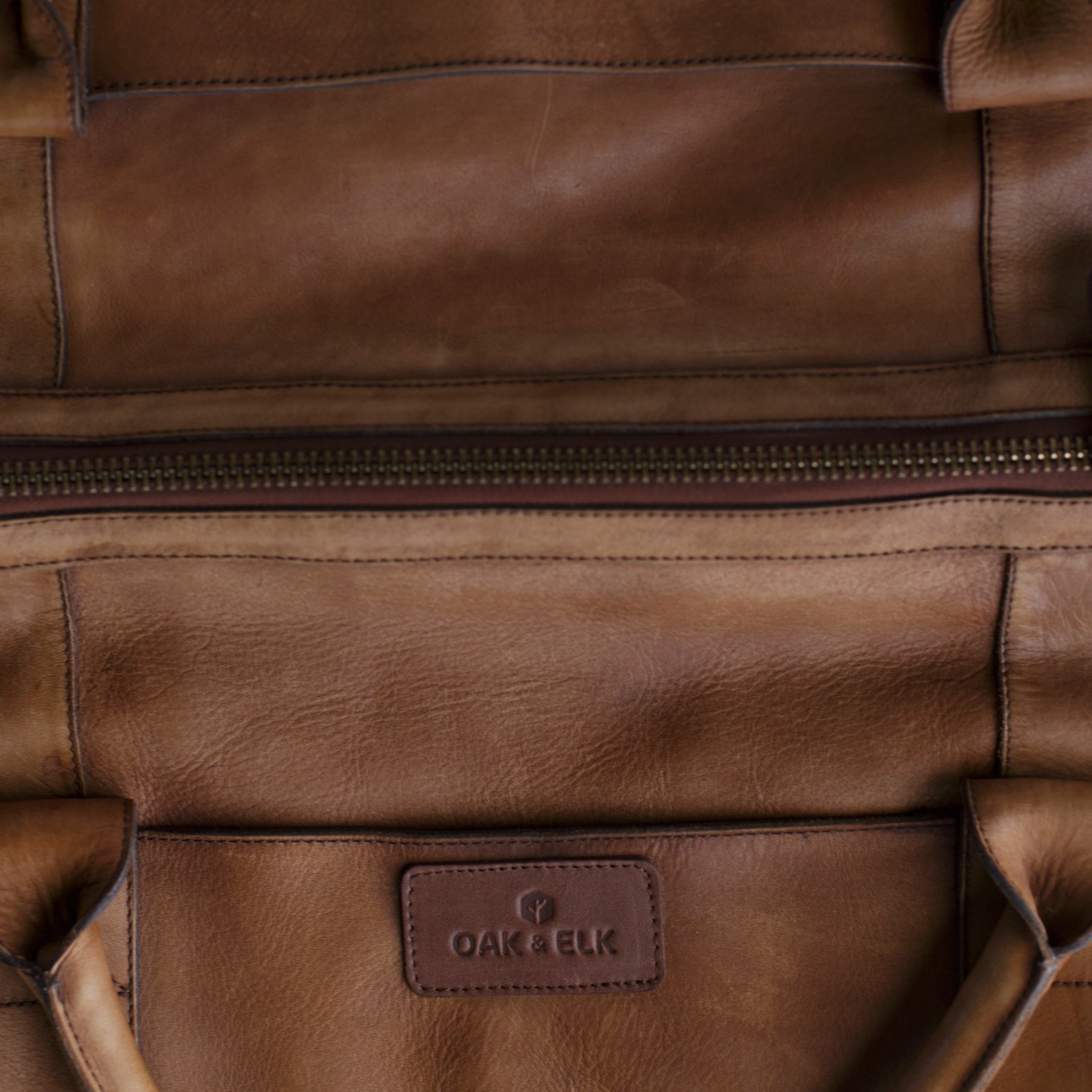 Leather duffel bag made of top-grain leather with smooth zipper, structured body, interior pockets, and adjustable strap