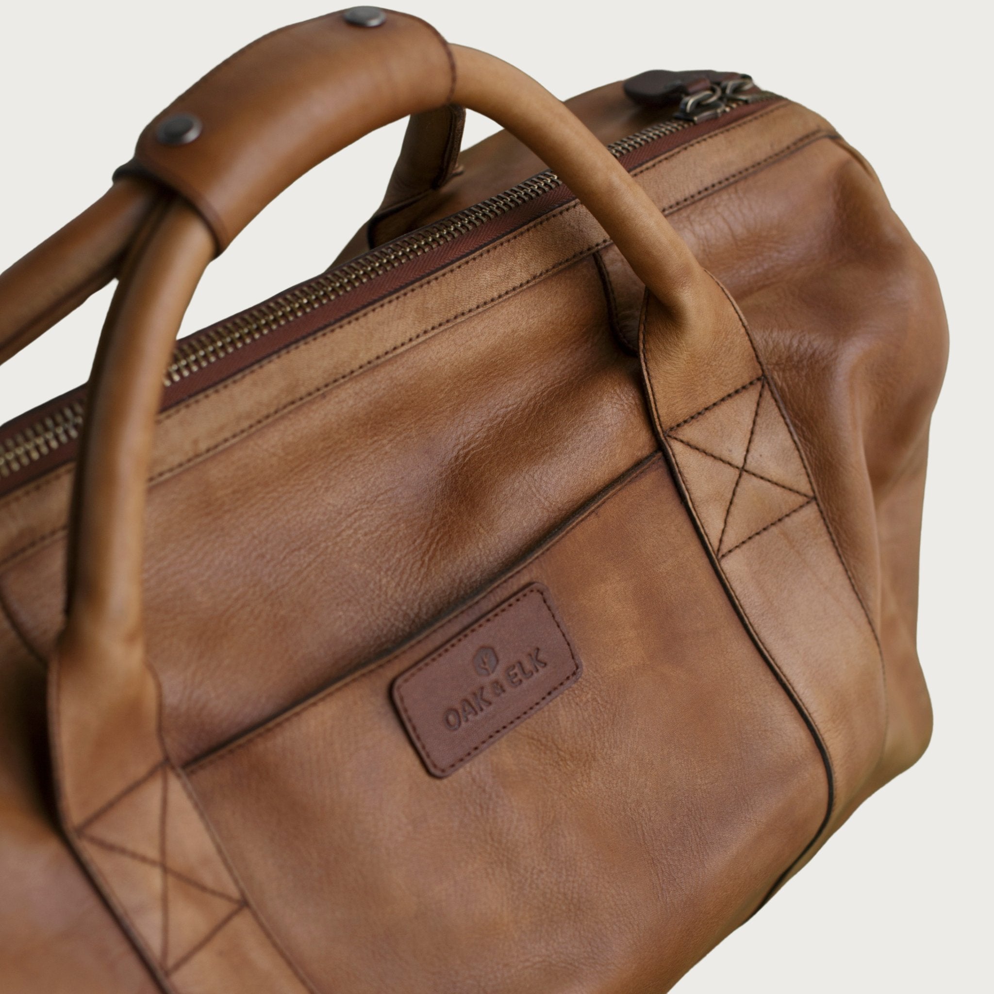 Leather duffel bag made of top-grain leather with smooth zipper, structured body, interior pockets, and adjustable strap