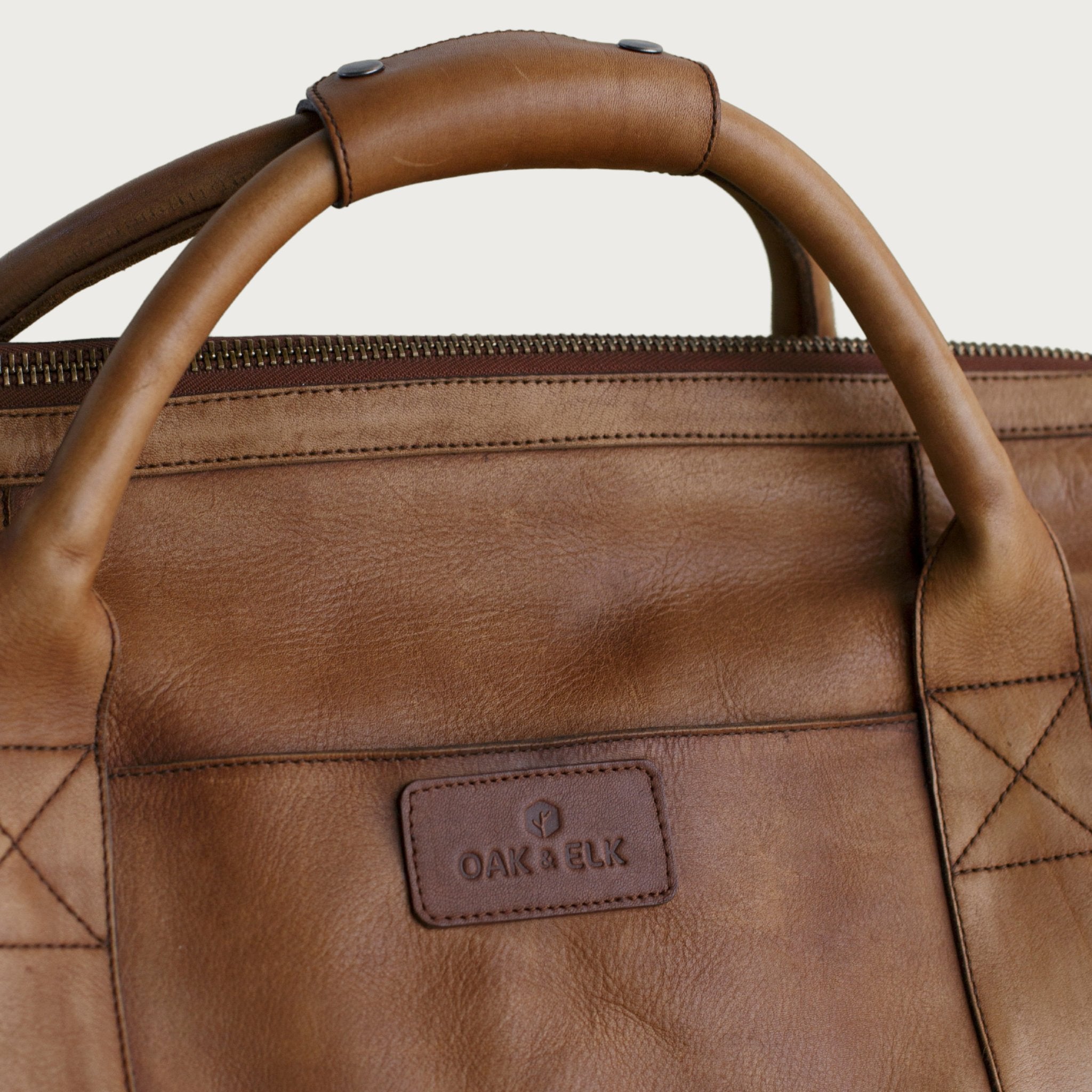 Leather duffel bag made of top-grain leather with smooth zipper, structured body, interior pockets, and adjustable strap