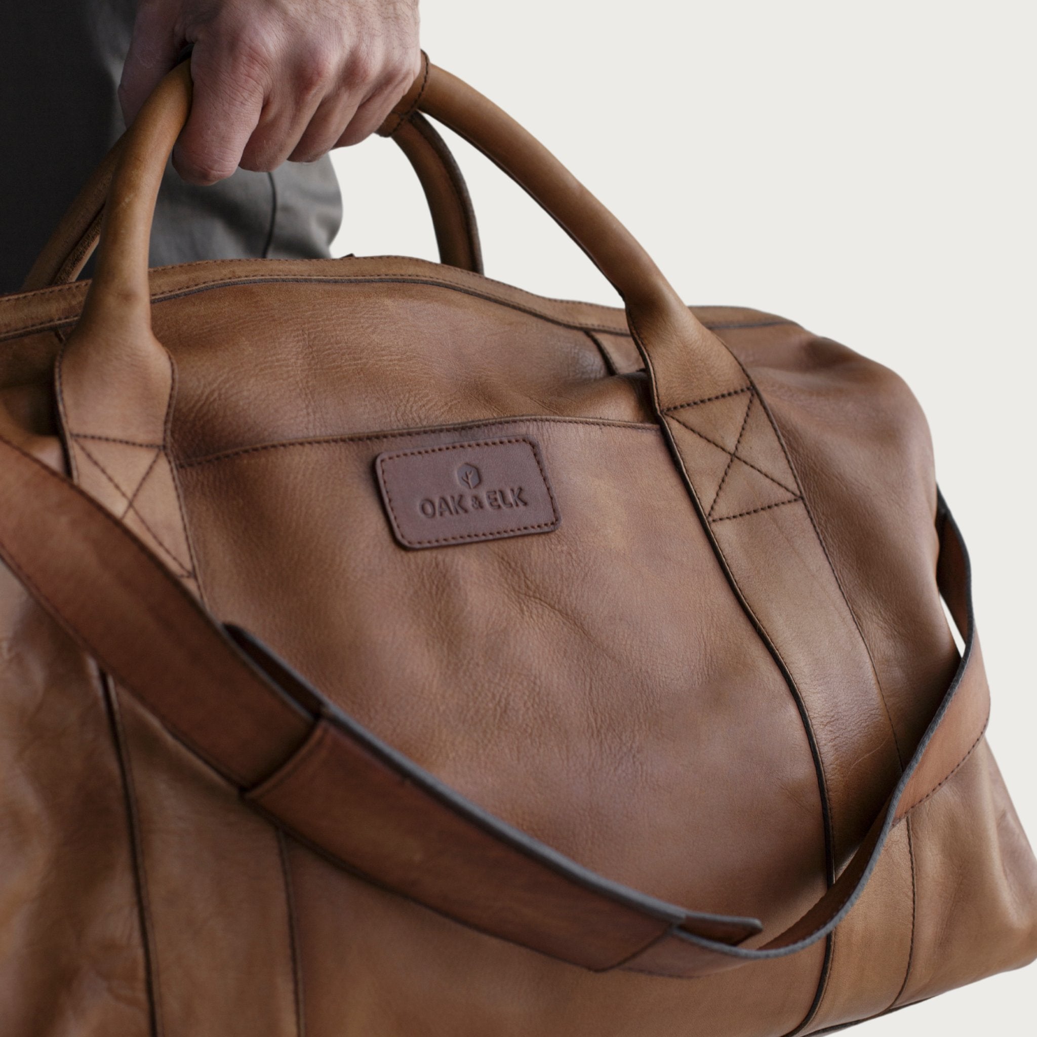 Leather duffel bag made of top-grain leather with smooth zipper, structured body, interior pockets, and adjustable strap