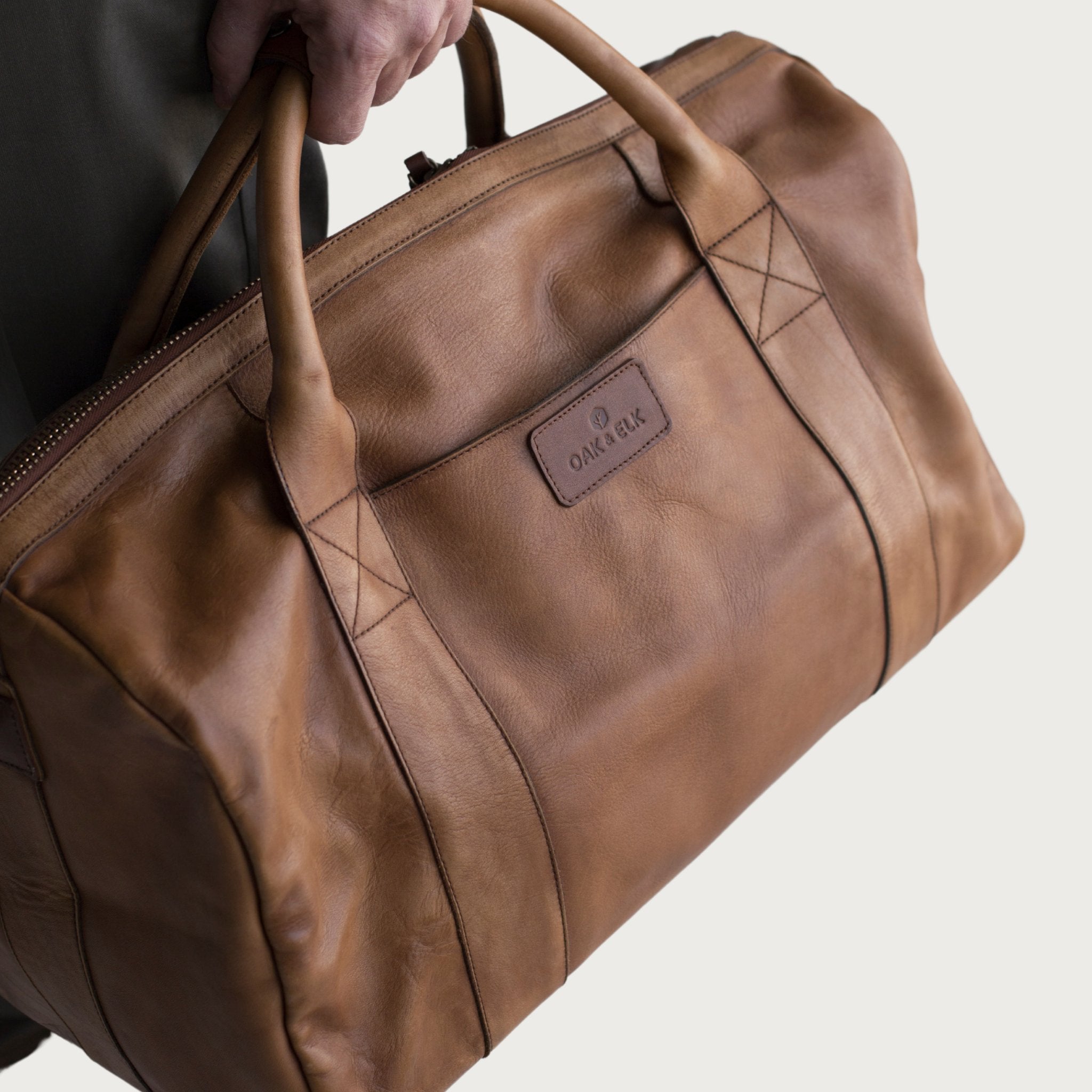 Leather duffel bag made of top-grain leather with smooth zipper, structured body, interior pockets, and adjustable strap