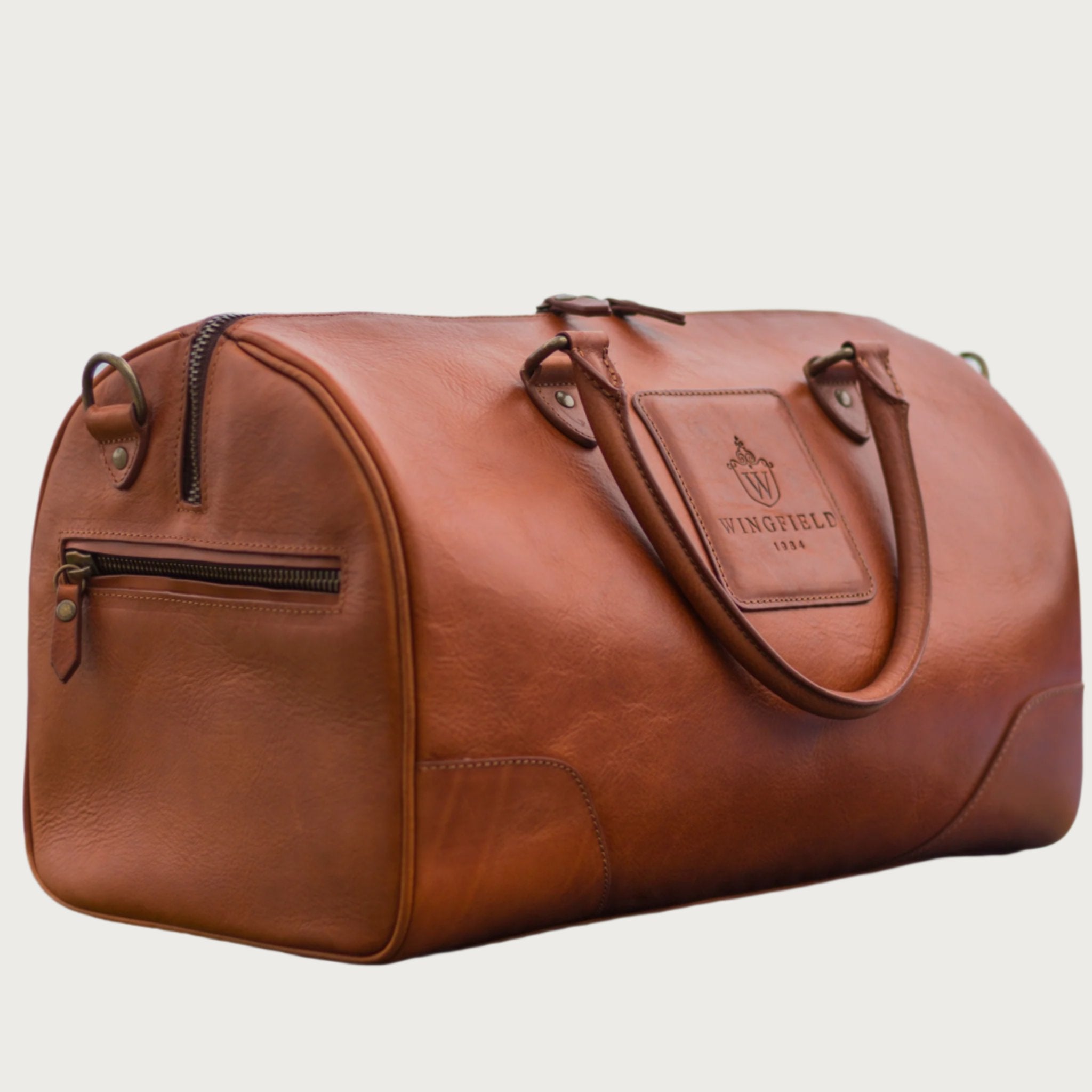 Full-grain leather duffel bag with zip closure, structured shape, carry handles, and adjustable shoulder strap, compact sleek