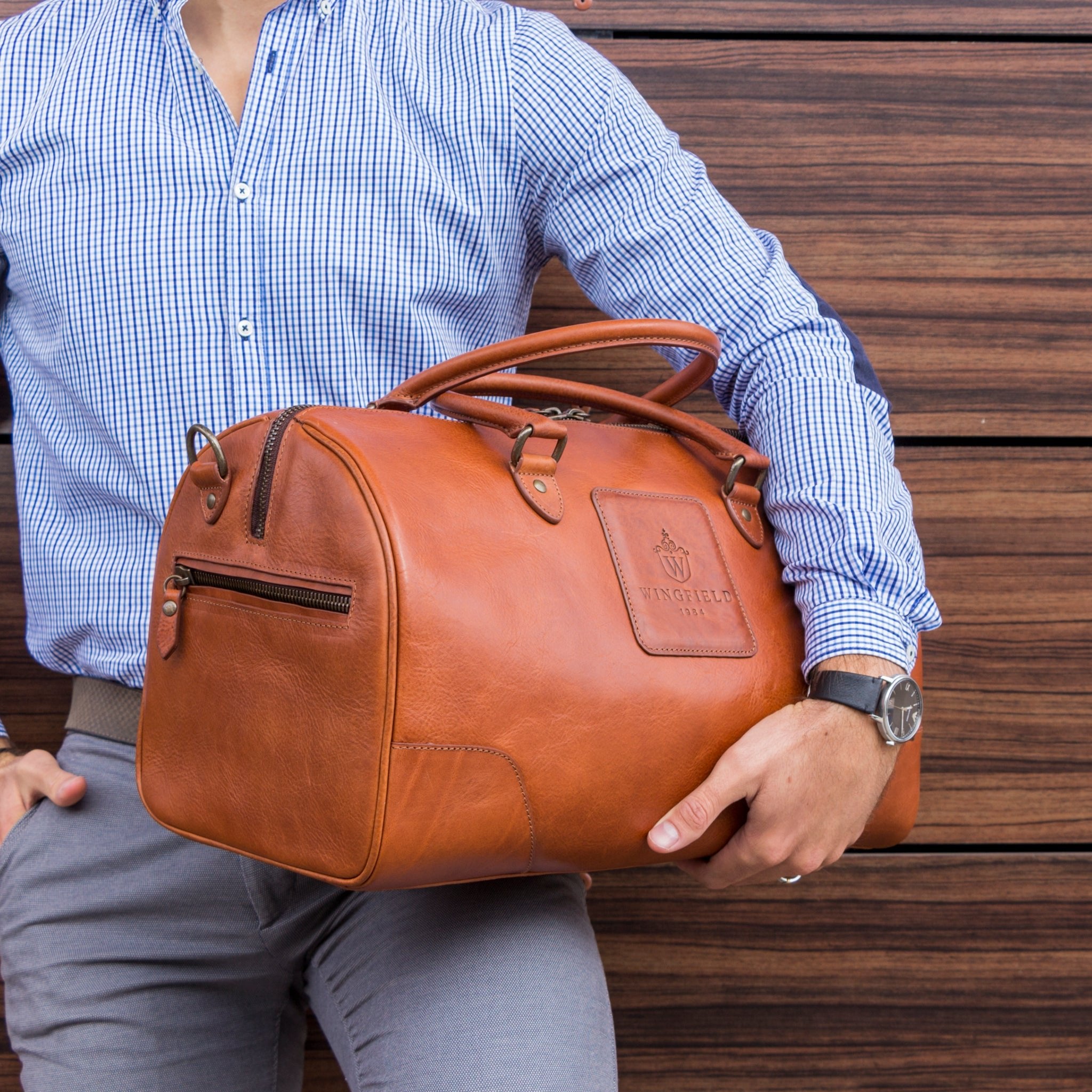 Full-grain leather duffel bag with zip closure, structured shape, carry handles, and adjustable shoulder strap, compact sleek