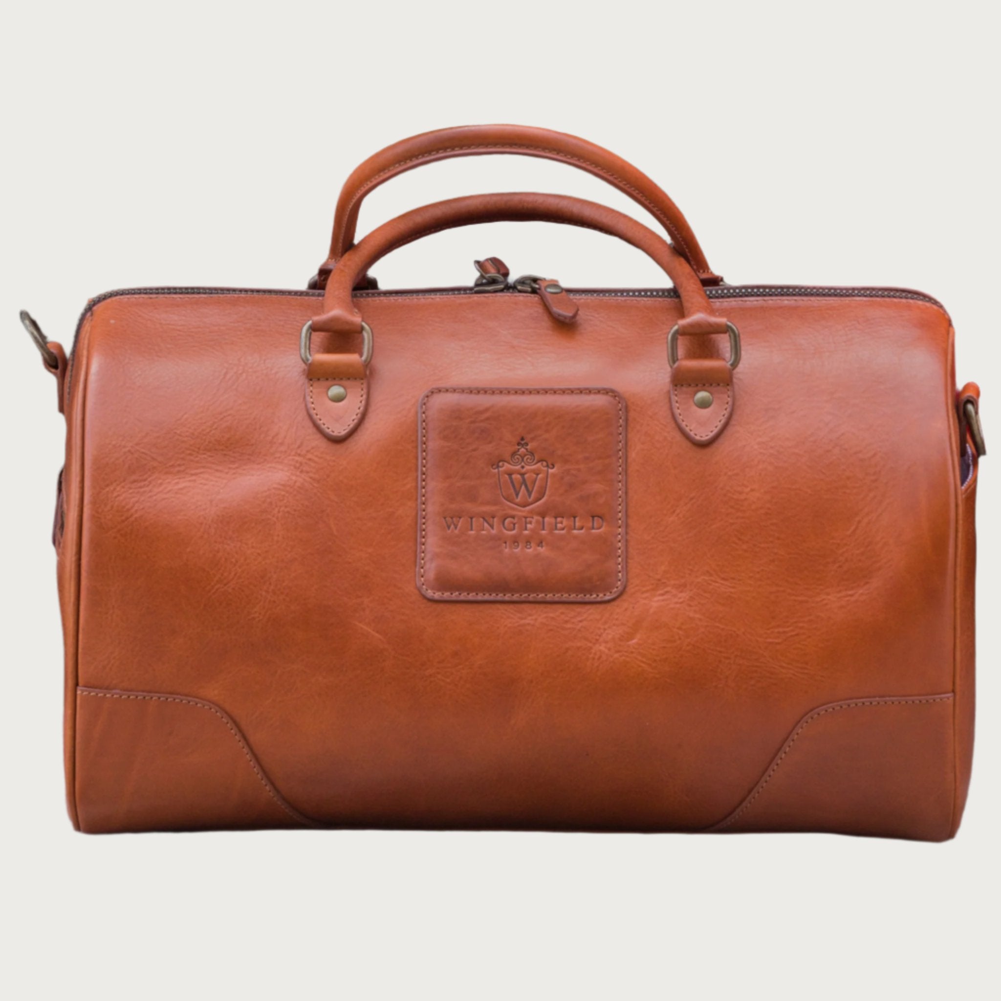 Full-grain leather duffel bag with zip closure, structured shape, carry handles, and adjustable shoulder strap, compact sleek