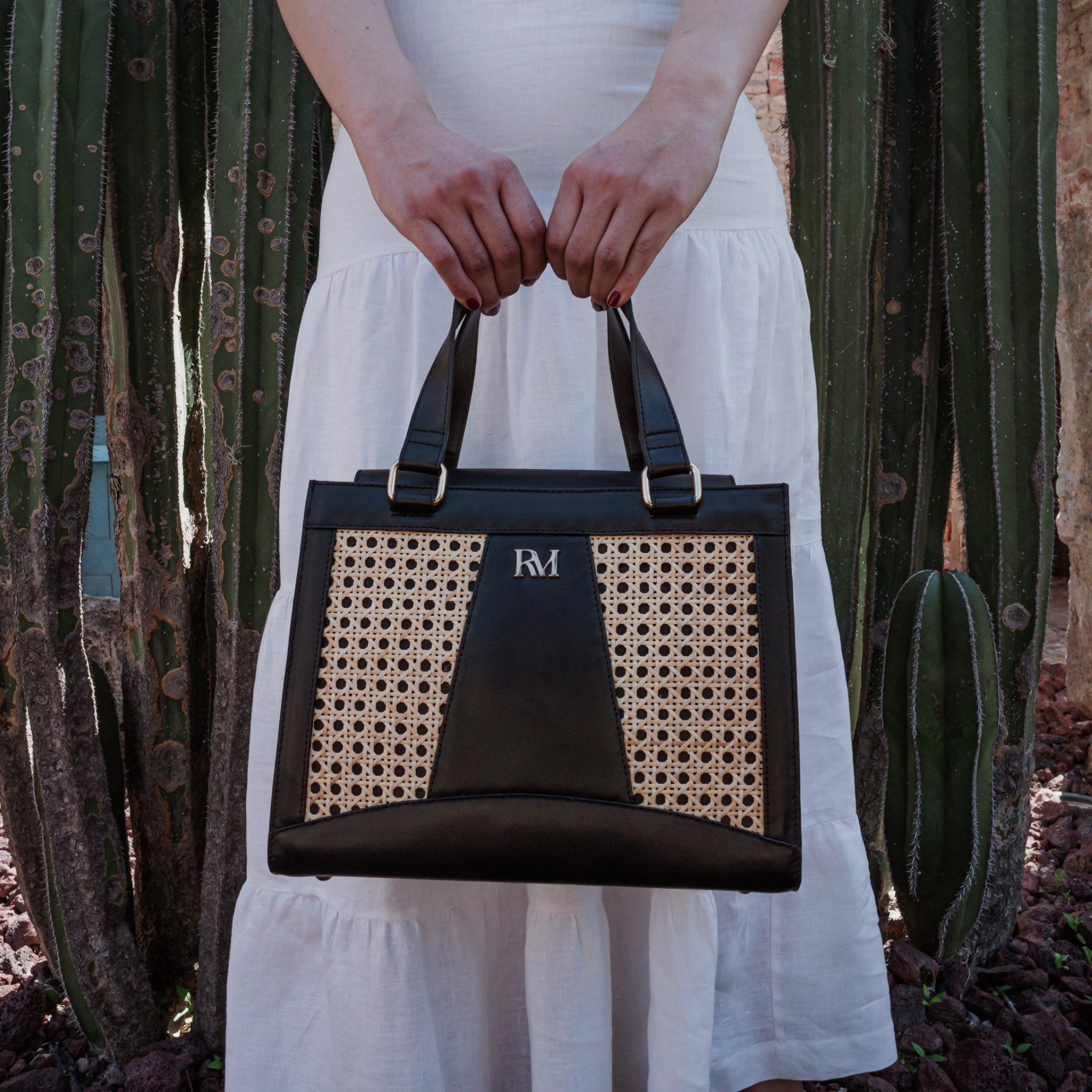 Wicker and black leather tote bag with structured silhouette, cutout handles, inner lining, and artisanal woven texture.