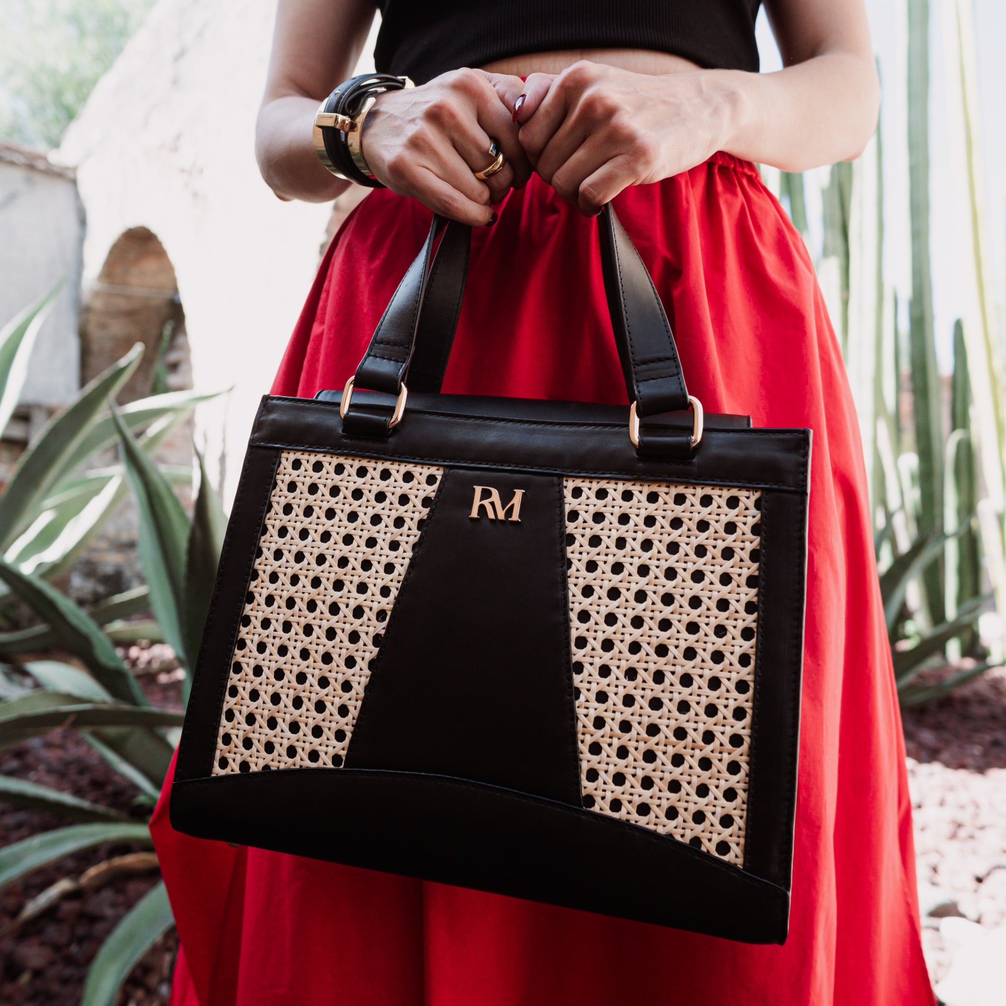 Wicker and black leather tote bag with structured silhouette, cutout handles, inner lining, and artisanal woven texture.