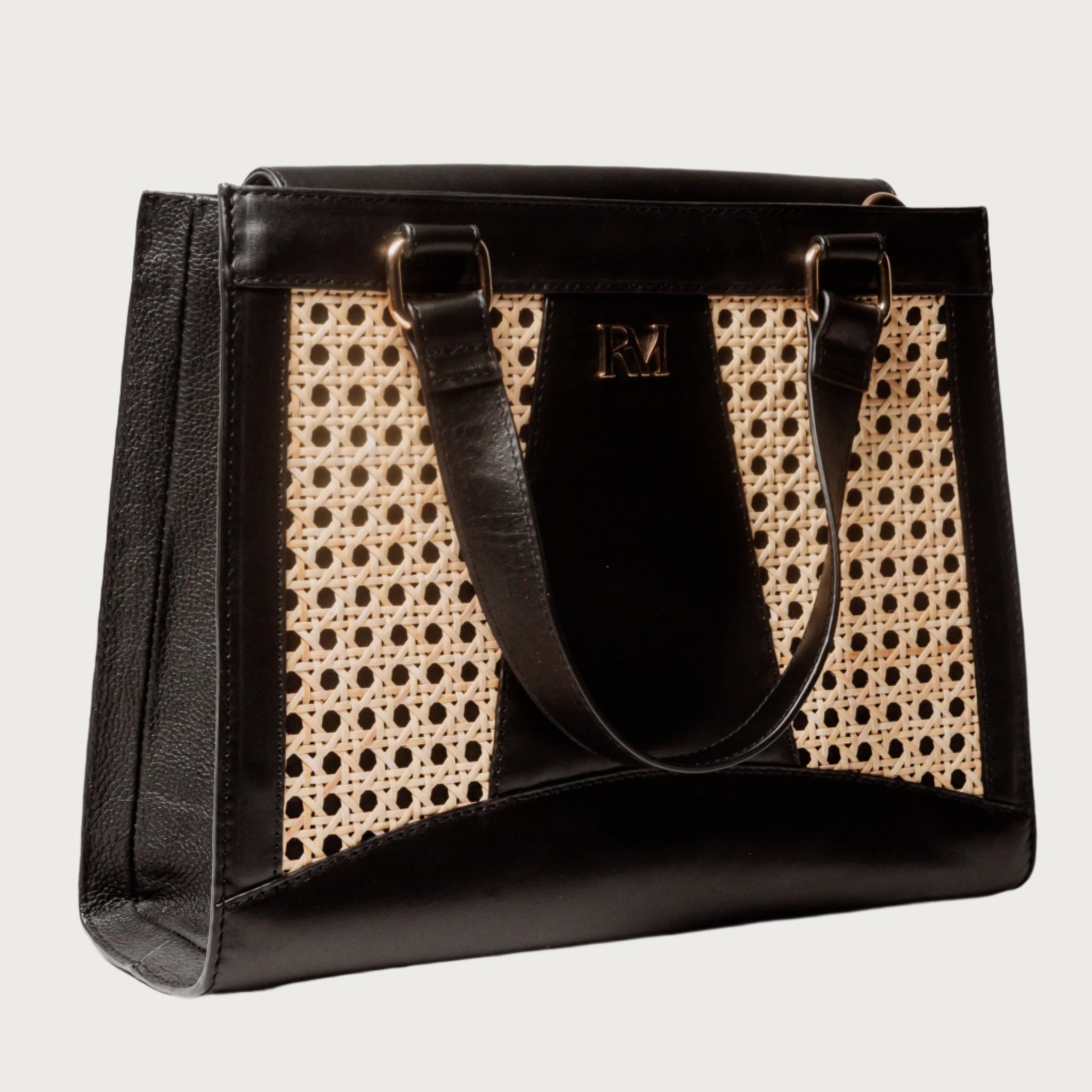 Wicker and black leather tote bag with structured silhouette, cutout handles, inner lining, and artisanal woven texture.