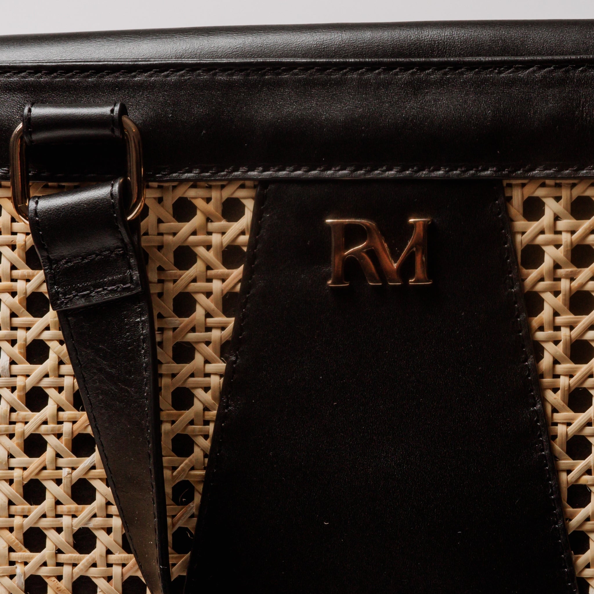 Wicker and black leather tote bag with structured silhouette, cutout handles, inner lining, and artisanal woven texture.