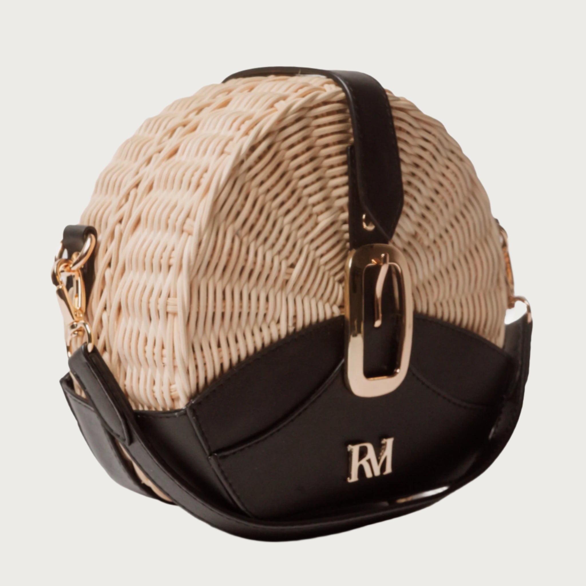 Round wicker and black leather crossbody bag with flap closure, gold chain strap, and structured shape unique eye-catching.