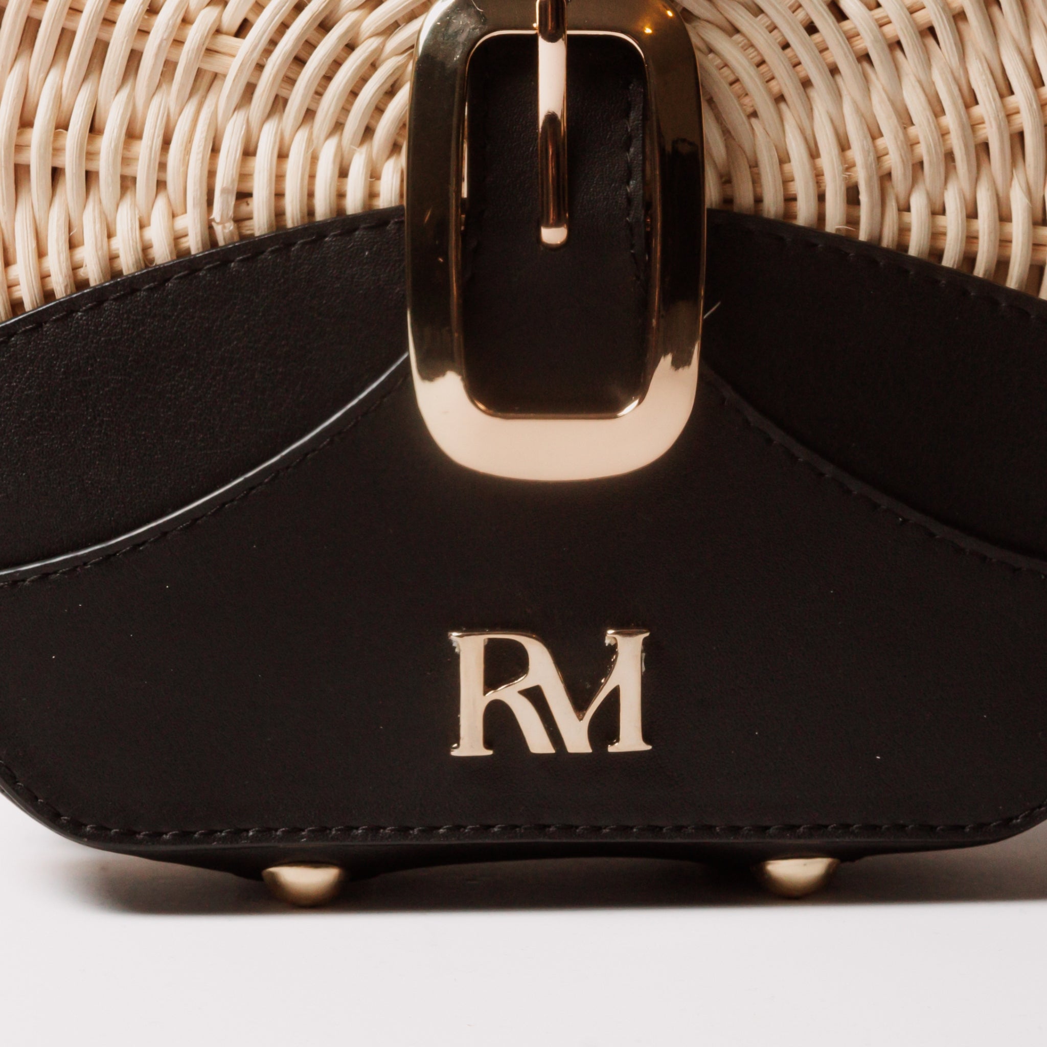 Round wicker and black leather crossbody bag with flap closure, gold chain strap, and structured shape unique eye-catching.