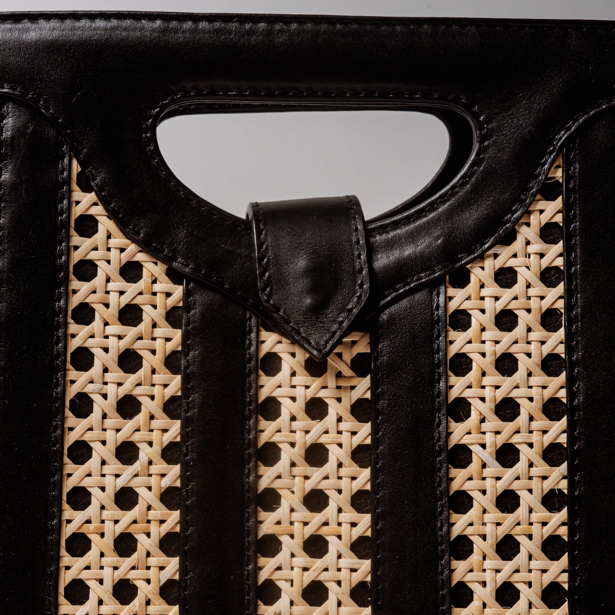 Handwoven wicker and black leather clutch with structured silhouette, cutout handle, and fabric lining bold elegant design