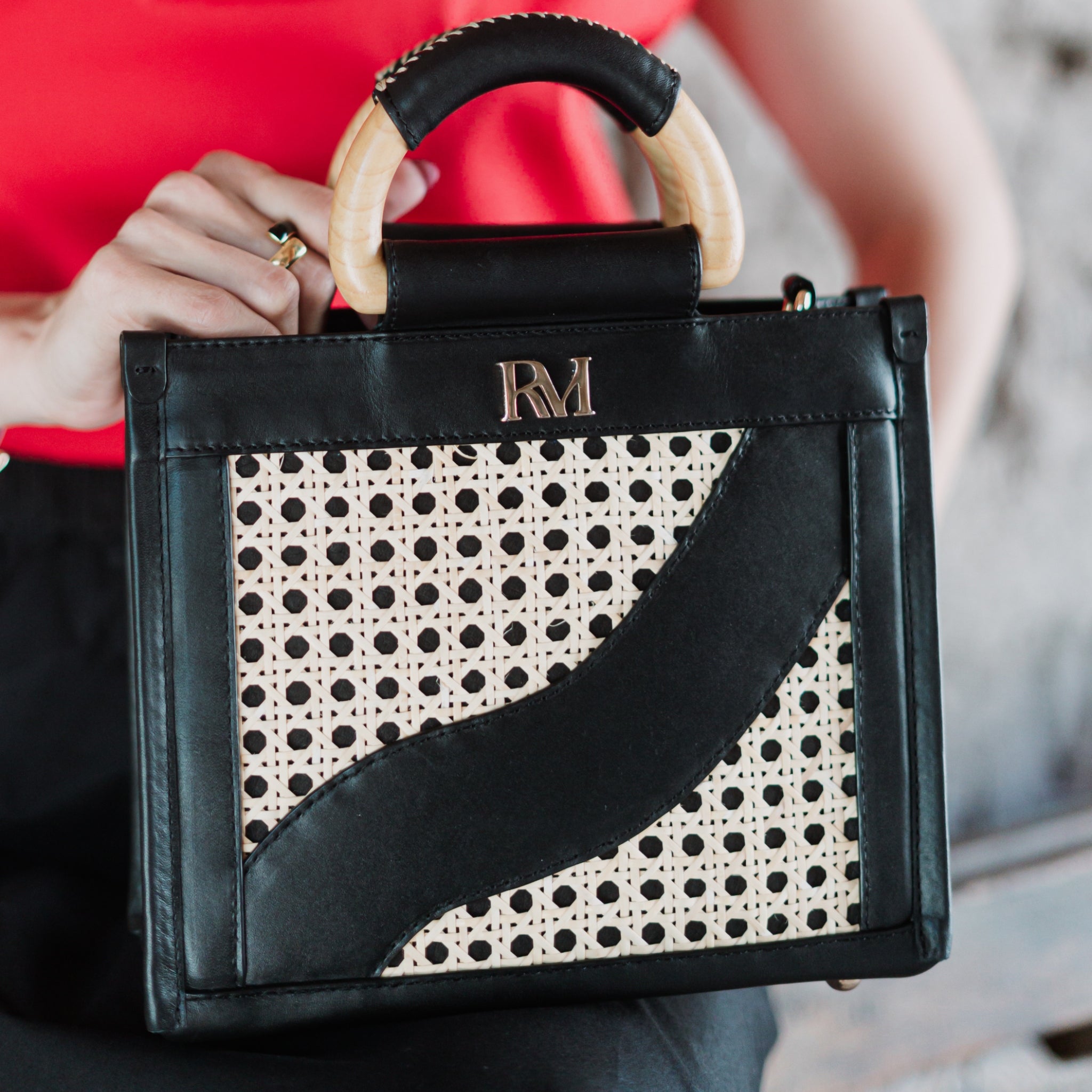 Structured square handbag with handwoven cane body, black leather trim, top handles, and crossbody strap — bold refined look