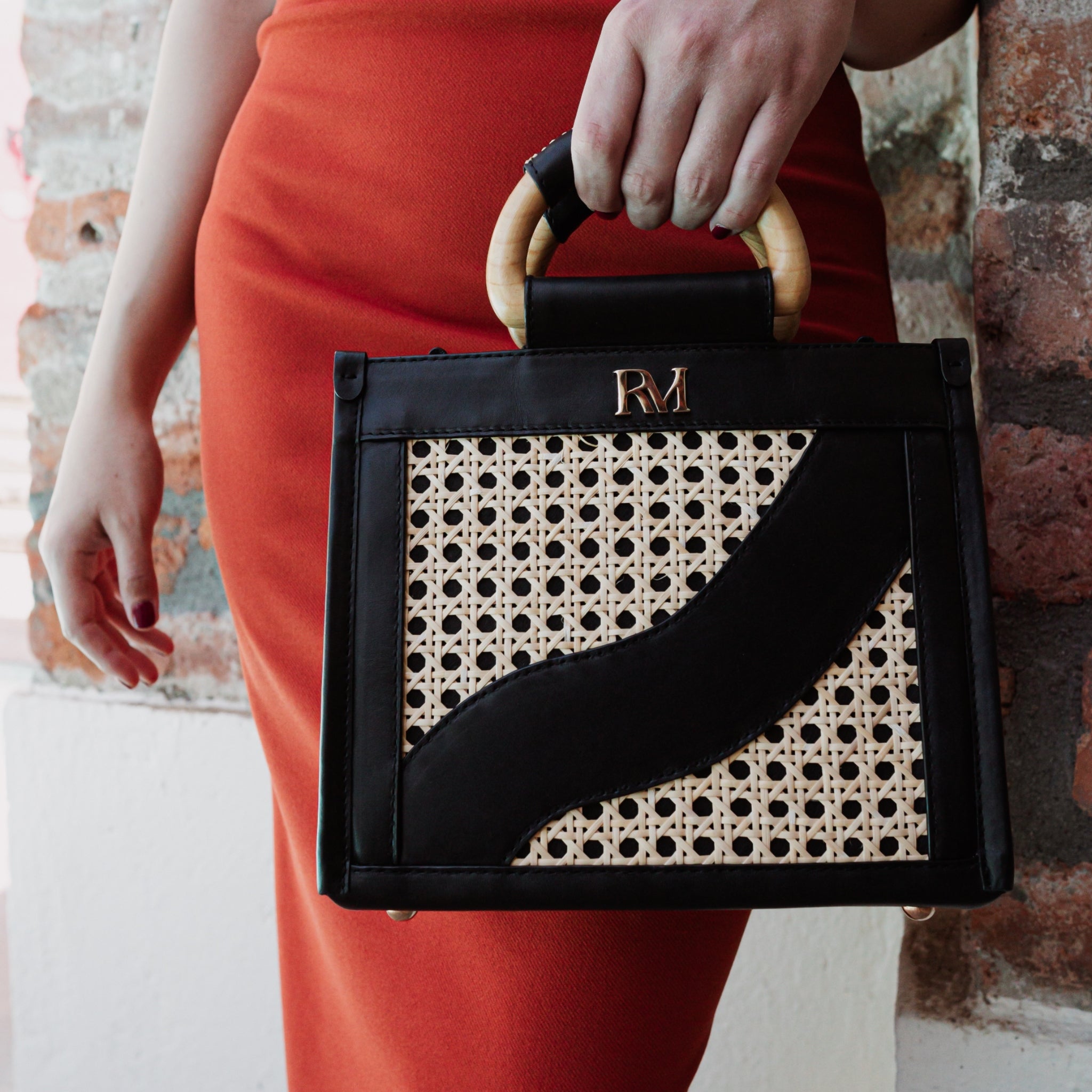 Structured square handbag with handwoven cane body, black leather trim, top handles, and crossbody strap — bold refined look