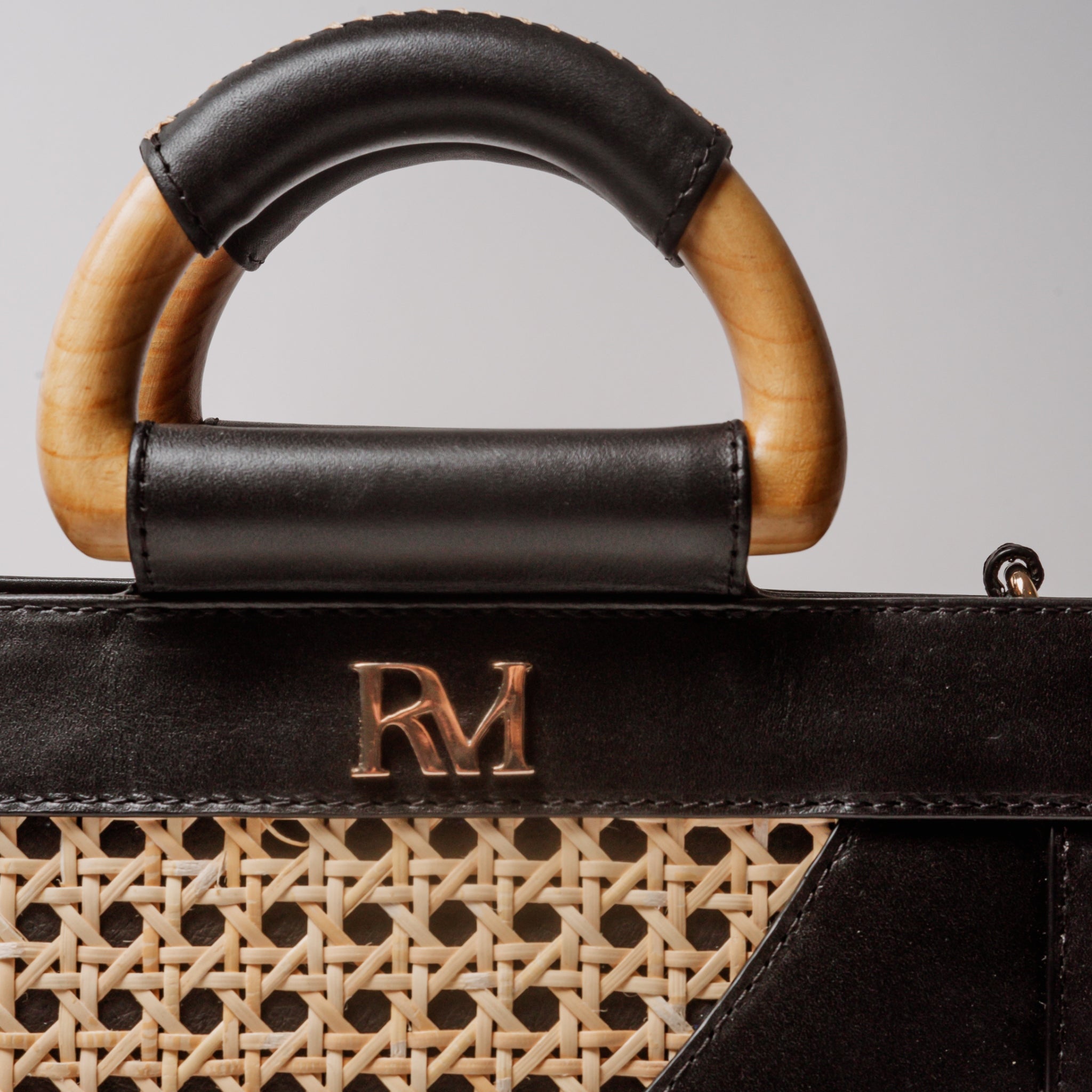 Structured square handbag with handwoven cane body, black leather trim, top handles, and crossbody strap — bold refined look