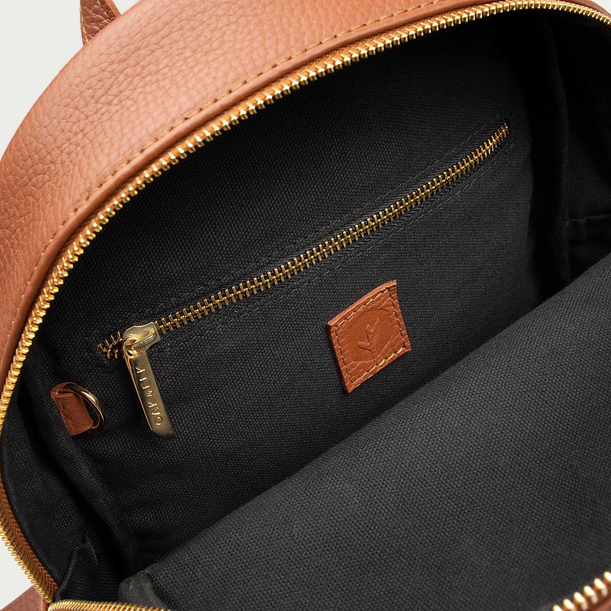 Leather backpack with smooth finish, adjustable straps, front zipper pocket, and gold hardware – Emma by OAK & ELK.