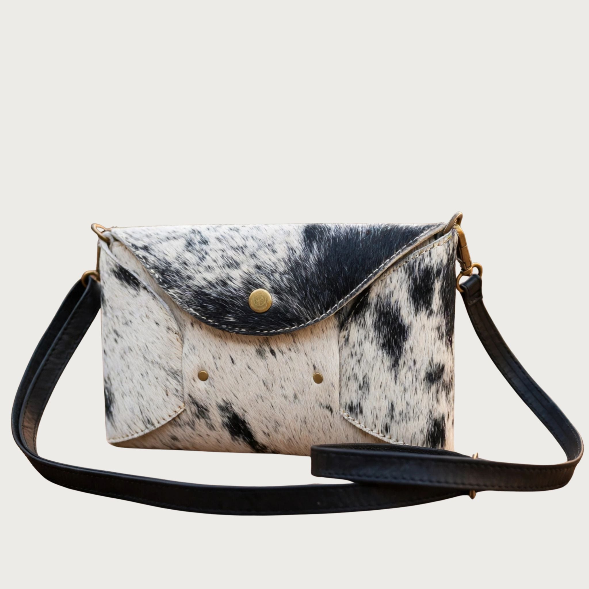 Front view of Oak & Elk handmade cowhide crossbody bag on white background, showing black-and-white hair-on-hide exterior and black leather strap